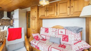 A cozy room with wooden cabinets, a sofa with patterned cushions, a chair with a red blanket, and a hanging light fixture. - CHALET DES CIMES - NOTRE DAME DU PRE (NOTRE DAME DU PRE)