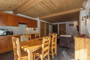 Une table à manger en bois avec des chaises, un coin cuisine avec des meubles en bois et un espace de vie chaleureux avec un canapé.
