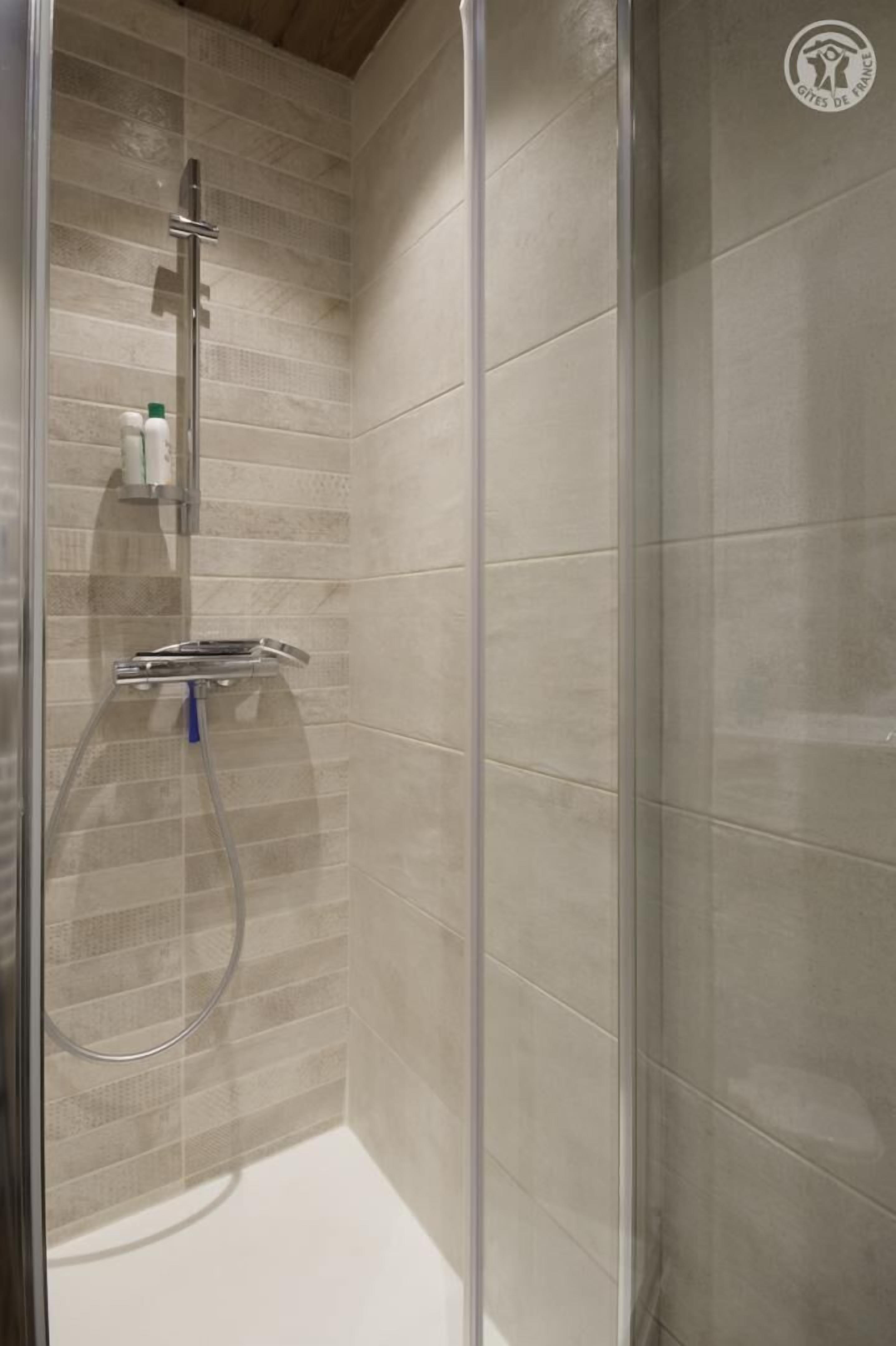 A glass-enclosed shower with beige tiles, a chrome showerhead, and a handheld showerhead.