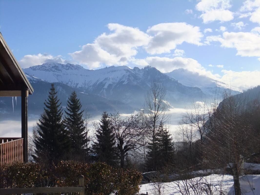 A mountain cabin with a view of snow-covered peaks and a forested valley.