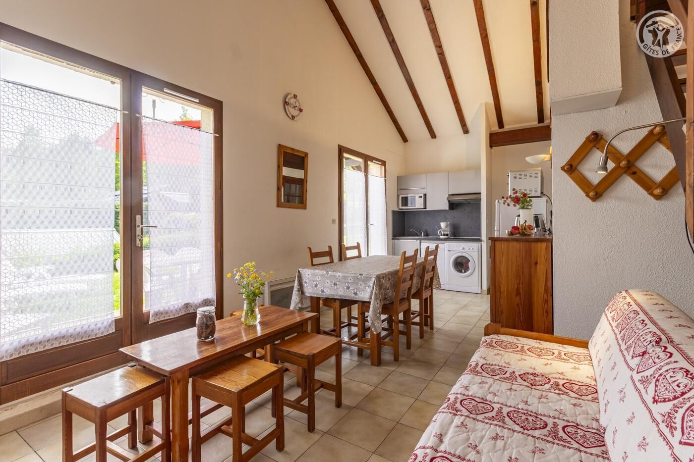 Een gezellige, goed verlichte kamer met een eettafel, stoelen, een bank en een keukenhoek met een wasmachine.
