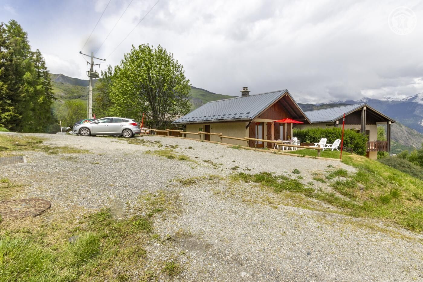 A rustic mountain lodge with a gravel driveway, a parked car, and outdoor seating.
