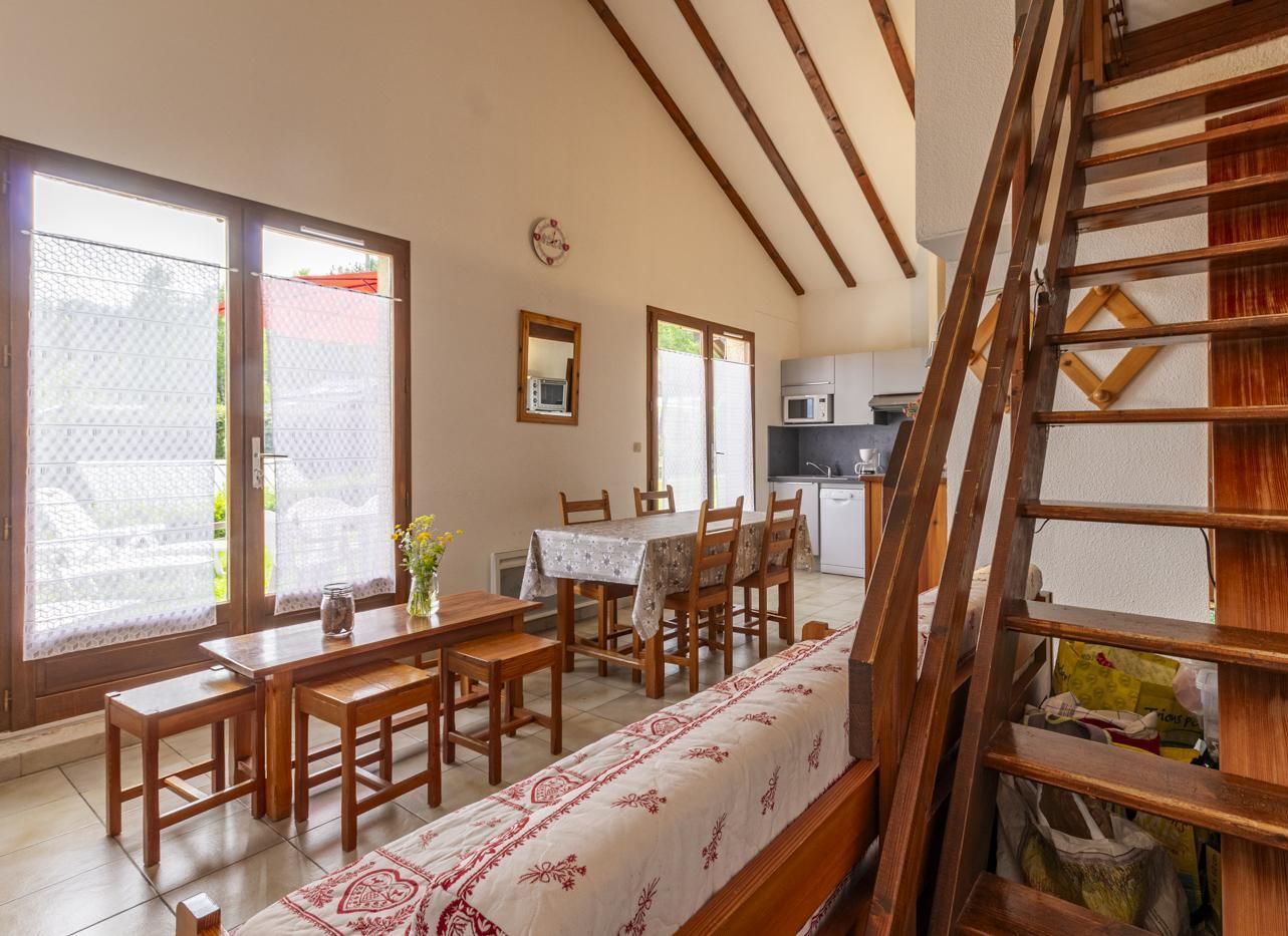 Un espace repas avec des tables et des chaises en bois, une cuisine à l’arrière-plan et un escalier avec des rampes en bois.