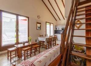 Un comedor con mesas y sillas de madera, una cocina al fondo y una escalera con barandillas de madera.