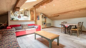 Un espacio habitable tipo loft acogedor con un sofá rojo, una mesa de comedor de madera y un techo alto con vigas a la vista.