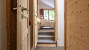 Un pasillo estrecho con paredes de madera y escaleras con alfombra que conducen a un dormitorio con cama y ventana.