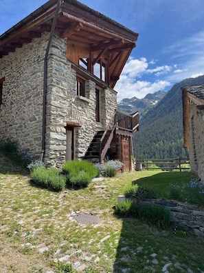 Un bâtiment en pierre doté d’un balcon en bois, d’un escalier et offrant une vue sur les montagnes.