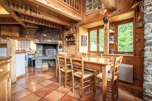 A rustic wooden interior with a stone fireplace, wooden dining table, and chairs.