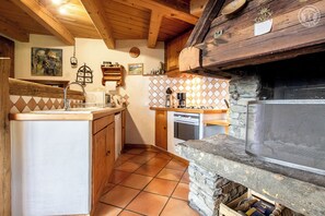 A rustic kitchen with a stone oven, wooden cabinets, and a tiled backsplash.