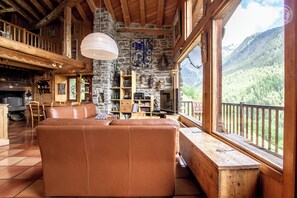 A cozy cabin interior with a leather sofa, wooden shelves, and a stone wall.