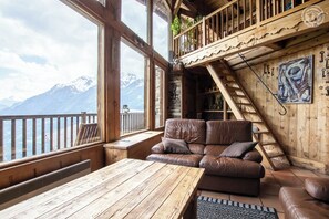 A wooden interior with a leather sofa, a wooden table, and a balcony overlooking mountains.
