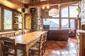 A wooden interior with a dining table, chairs, a sofa, and a stone wall.