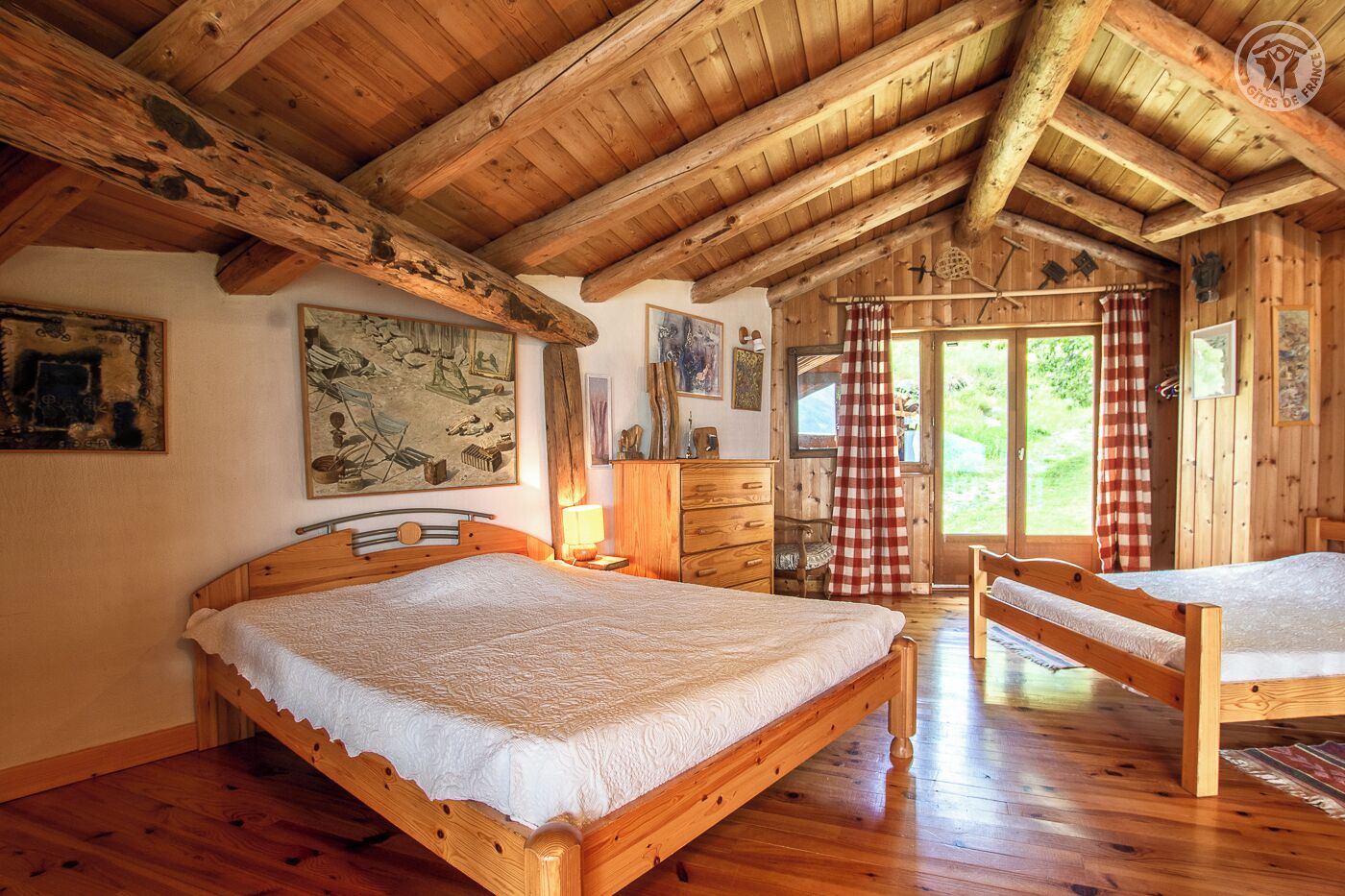 A wooden cabin with a high ceiling, a bed with a white bedspread, a wooden dresser, and a chair.