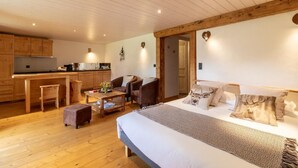 Ein gemütliches Zimmer mit einem Bett, einem Schreibtisch und einem Stuhl. Es gibt eine Küchenzeile mit Holzausbau und einem Spülbecken.