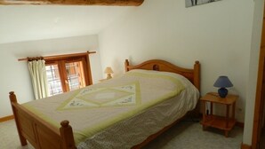 Une chambre à coucher avec un lit en bois, une fenêtre avec des rideaux, une table de chevet avec une lampe et un tableau accroché au mur.