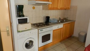Une cuisine compacte équipée d’un lave-linge, d’un four à micro-ondes, d’une cuisinière et de meubles de rangement en bois.