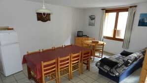 Un espace de vie compact comprenant une table et des chaises, un canapé, une petite kitchenette et une fenêtre avec des rideaux.