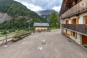 A mountain lodge with a stone facade, wooden balcony, and a view of a forested valley.