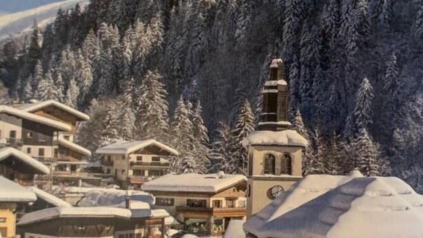En snötäckt by med traditionella byggnader, inklusive en framträdande kyrka med ett klocktorn.