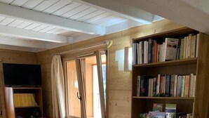 Ett mysigt vardagsrum med träpanel på väggarna, en bokhylla, två fåtöljer, ett litet bord och en tv.