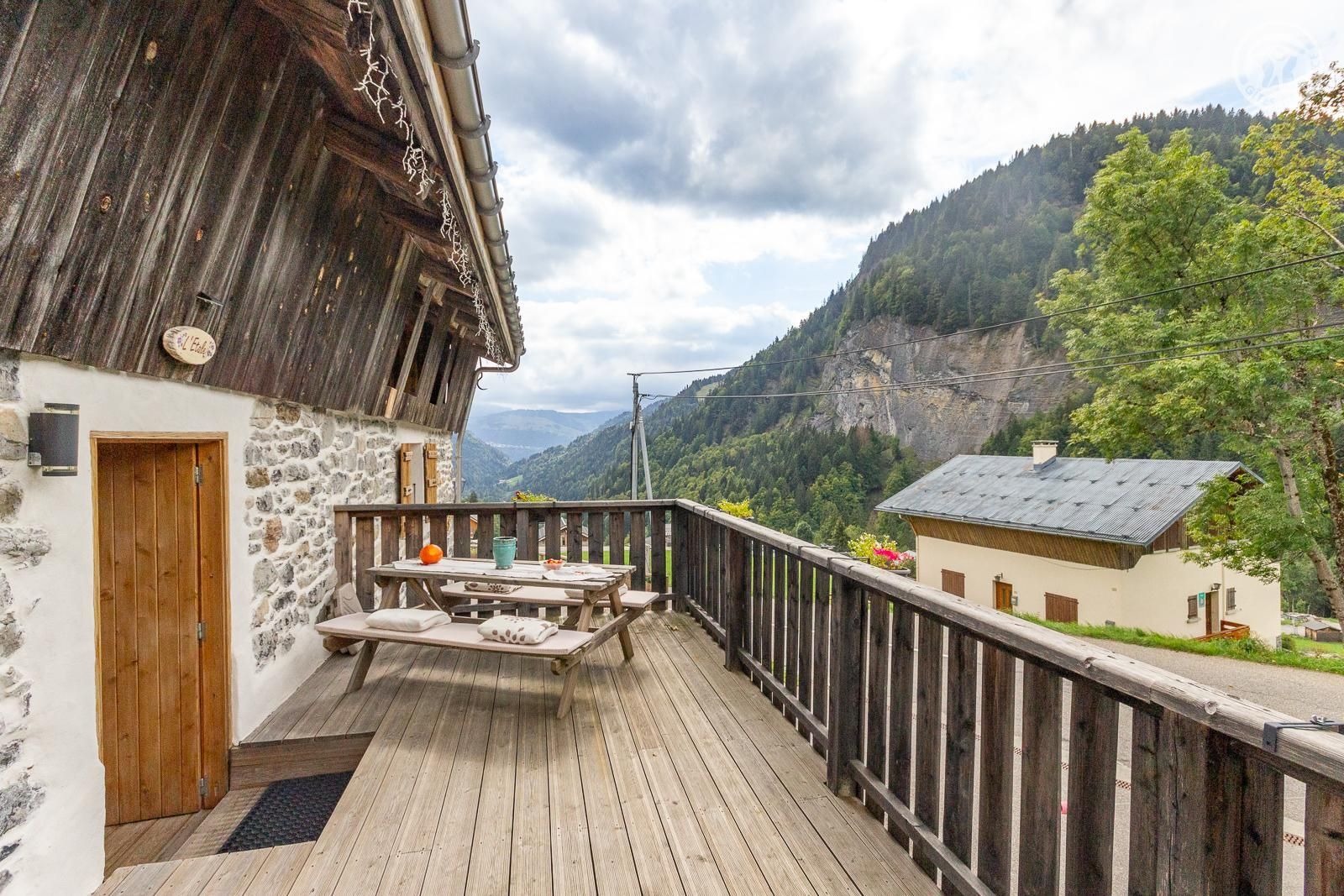 A wooden deck with a stone wall, a wooden door, and a table with a bench.