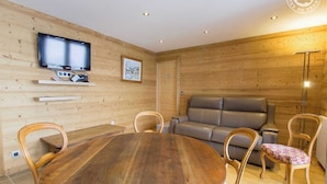 Una habitación acogedora con paredes de madera, una mesa redonda de madera, un sofá gris y un televisor montado en la pared.
