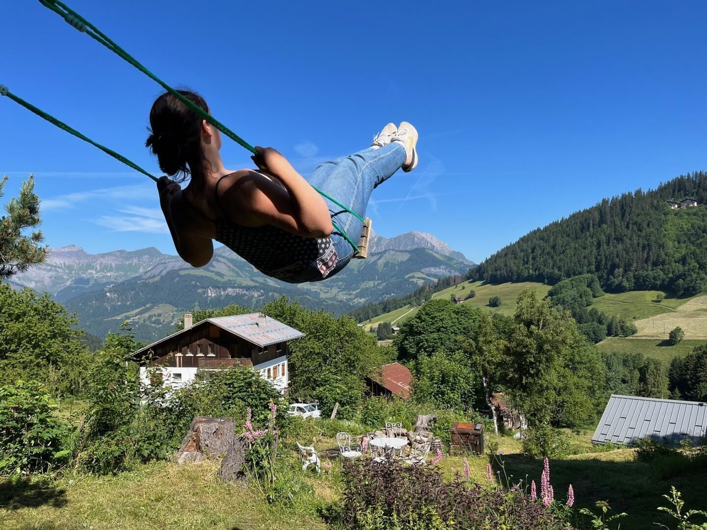 A person on a swing overlooking a mountainous landscape with houses and greenery.