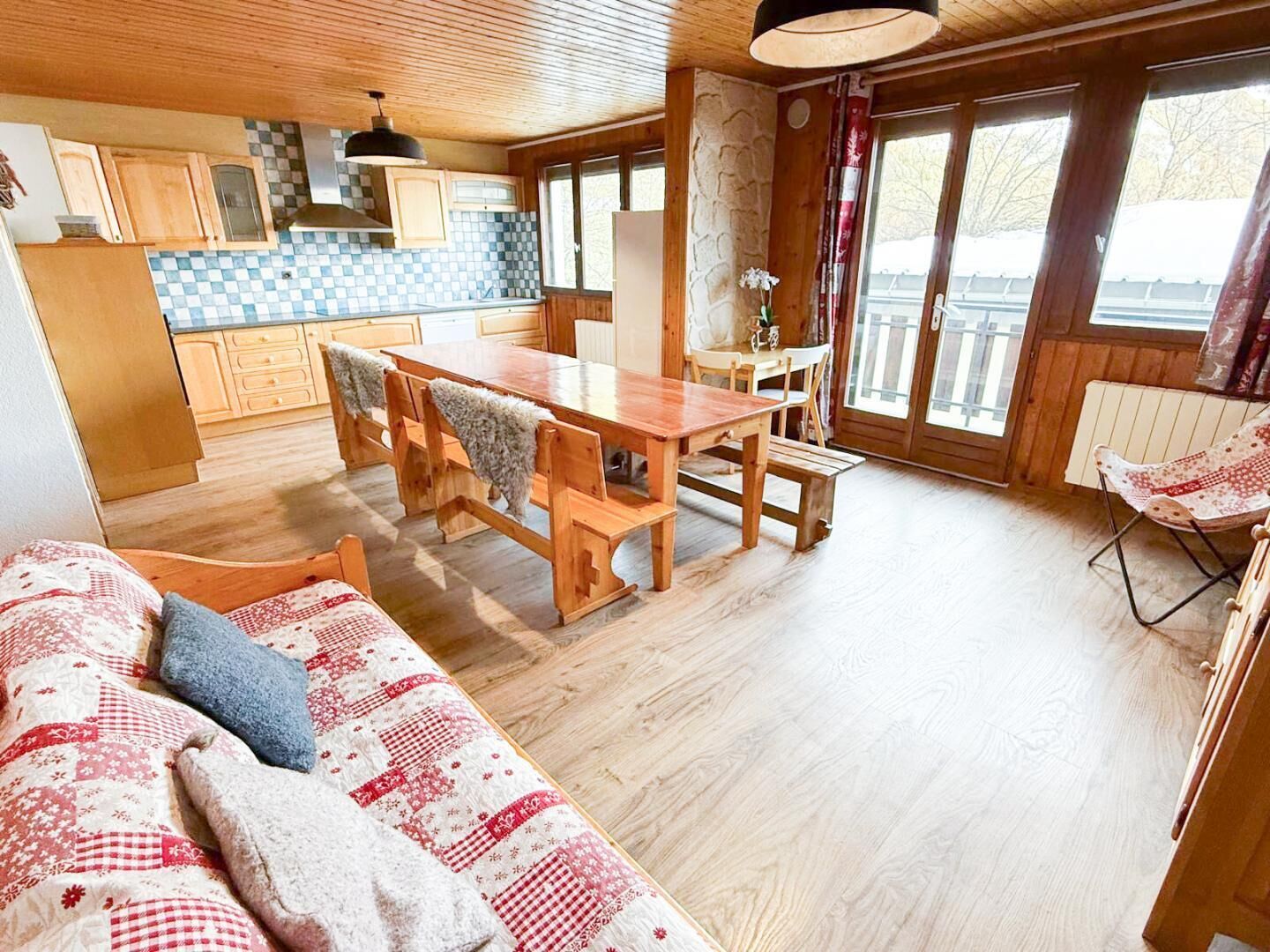 Ein gemütliches Blockhaus-Interieur mit einem Holzespeisetisch, Bänken, einer Couch und einer Küchenzeile mit Holzschränken und einer karierten Spritzschutzwand.