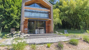 Eine moderne Holzhütte mit großer Glasscheibe, umgeben von einem Garten mit Blumen und Rasen.