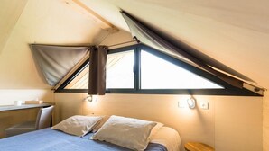 Ein Schlafzimmer mit schrägem Dach, einem Bett mit Kissen, einem kleinen Tisch und einem Hocker.