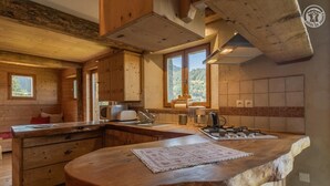 A rustic kitchen with wooden cabinets, a large island with a rug, and a view of the outdoors through the windows. - LA VARNIERE - BEAUFORT ARECHES (BEAUFORT ARECHES)