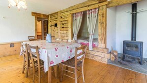 A rustic wooden room with a dining table, chairs, a fireplace, and a window with curtains. - LA VARNIERE - BEAUFORT ARECHES (BEAUFORT ARECHES)