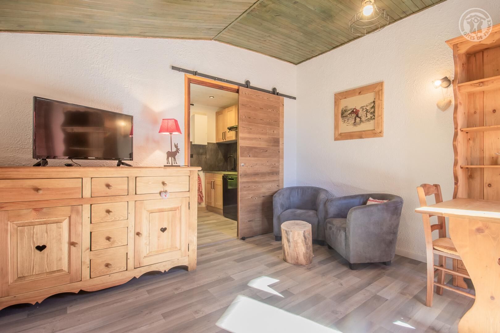 Une pièce confortable avec un meuble en bois, une télévision, une lampe rouge et un coin salon comprenant une table et des chaises.