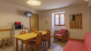 Una habitación compacta con una mesa de comedor de madera, sillas, una pequeña kitchenette con microondas y un televisor.