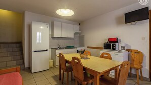 Una cocina compacta con armarios blancos, microondas, cafetera y una mesa de comedor con sillas de madera.