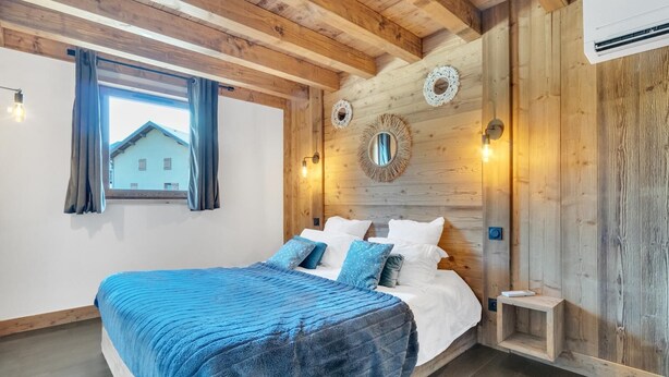 A bedroom with a wooden ceiling, a large bed with blue bedding, a window with curtains, and wall-mounted lights. - LA GRANGE A ROGER - MYANS (MYANS)