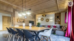 A dining area with a wooden table and chairs, a television, and a wall-mounted shelf with decorative items. - LA GRANGE A ROGER - MYANS (MYANS)