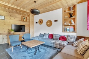 A cozy living room with a wooden ceiling, a large TV, a blue sofa, a wooden coffee table, and a bookshelf with decorative items. - LA GRANGE A ROGER - MYANS (MYANS)