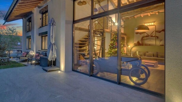 Een modern gebouw met grote glasramen, een overdekt terras en een zichtbare trap die naar een hoger gelegen verdieping leidt.