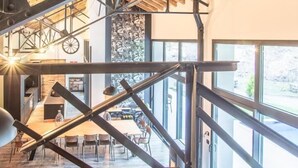 Een ruim interieur met een hoge plafond, zichtbare houten balken en een moderne trap.