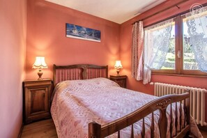 Ein Schlafzimmer mit einem hölzernen Bett, zwei Nachttischlampen, einer Heizung und einem Fenster mit Spitzenvorhängen.