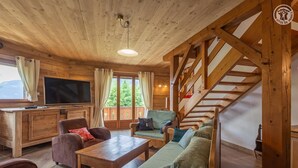 A cozy wooden interior with a sofa, chairs, a TV, and a staircase. - CHALET WAPITI - NOTRE DAME DE BELLECOMBE (NOTRE DAME DE BELLECOMBE)