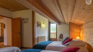 A bedroom with two beds, wooden ceiling beams, a radiator, a chair, and a window with a view of greenery. - CHALET WAPITI - NOTRE DAME DE BELLECOMBE (NOTRE DAME DE BELLECOMBE)