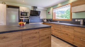 A modern kitchen with wooden cabinets, a built-in oven, a microwave, and a large window with a view of greenery. - CHALET WAPITI - NOTRE DAME DE BELLECOMBE (NOTRE DAME DE BELLECOMBE)