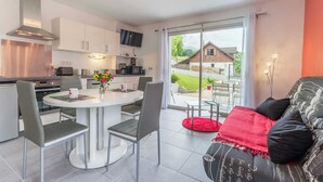A modern kitchen with white cabinets, a dining table with chairs, and a TV mounted above the counter.