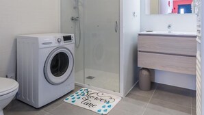 A modern bathroom with a washing machine, a glass-enclosed shower, and a vanity with a mirror.
