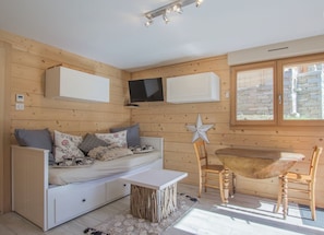 A cozy room with a wooden wall, a white sofa, a small table, and a TV mounted above the sofa.