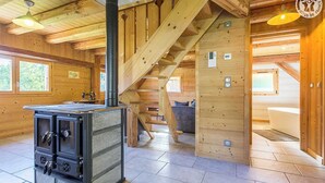 Et interiør af en hytte med brændeovn, trappe og udsigt til omgivelserne.