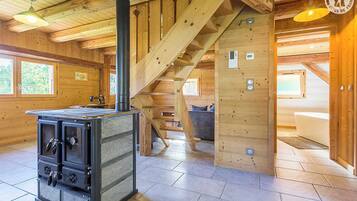 L’intérieur d’une cabane en rondins, avec un poêle à bois, un escalier et une vue sur l’extérieur.