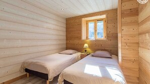 Et træhytteværelse med to senge, et vindue og et natbord med en lampe.
